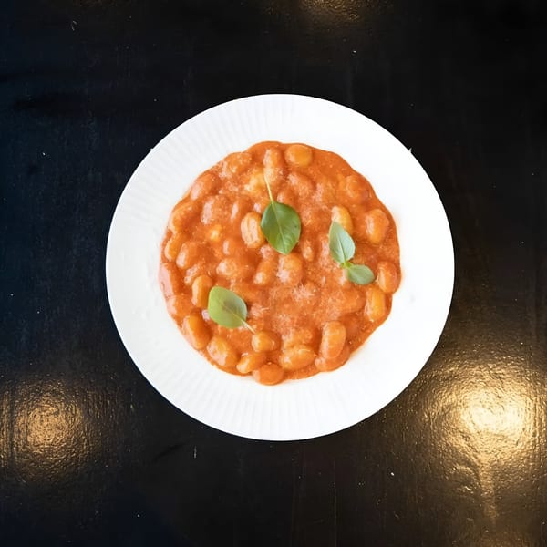 BASTA Pasteria's gnocchi in a rich tomato sauce, garnished with fresh basil leaves on a white plate.