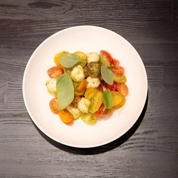 Colorful cherry tomato and mozzarella salad with fresh basil leaves on a white plate.