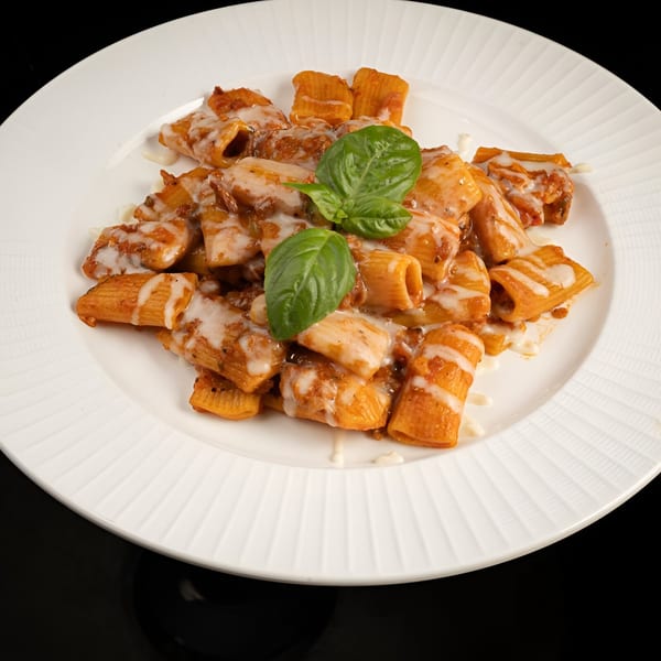 BASTA Pasteria's rigatoni pasta with creamy sauce and fresh basil on a white plate.