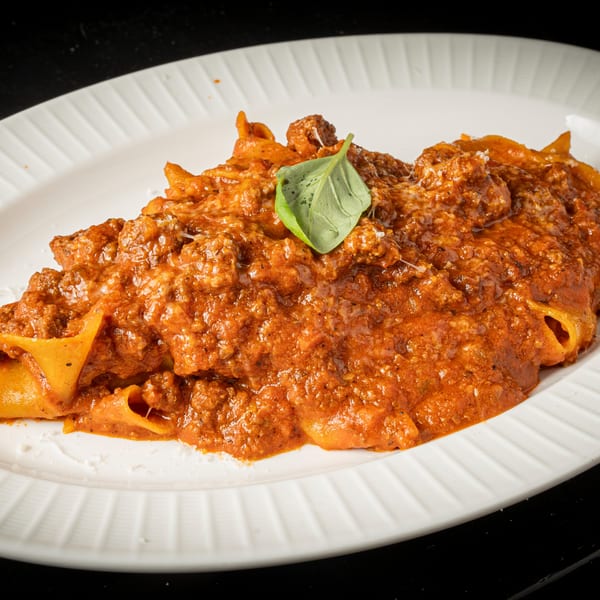 BASTA Pasteria's pappardelle pasta with a rich bolognese sauce, topped with grated cheese and a basil leaf.
