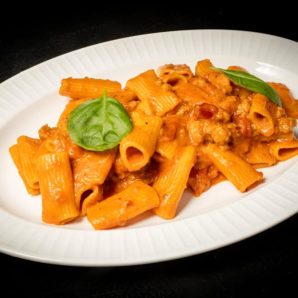 Rigatoni pasta with a creamy tomato sauce and fresh basil on a white plate.