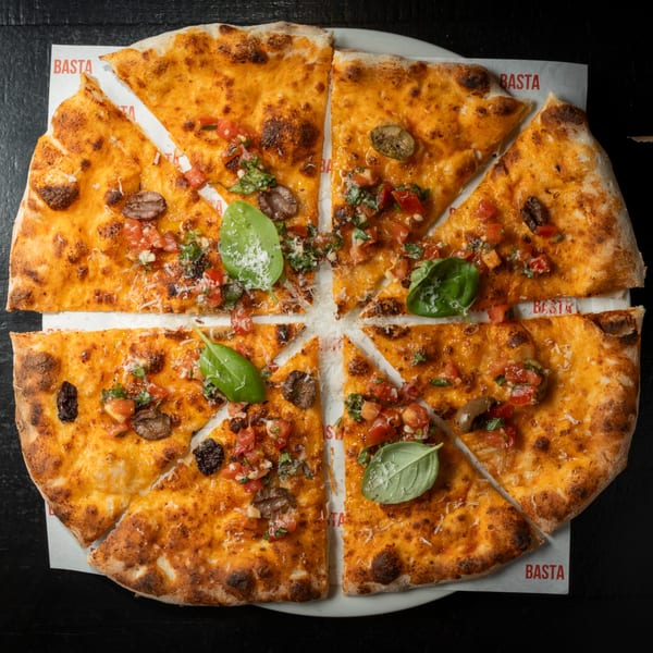BASTA Pasteria's sliced pizza with tomato, mushroom, basil, and cheese on a white plate.
