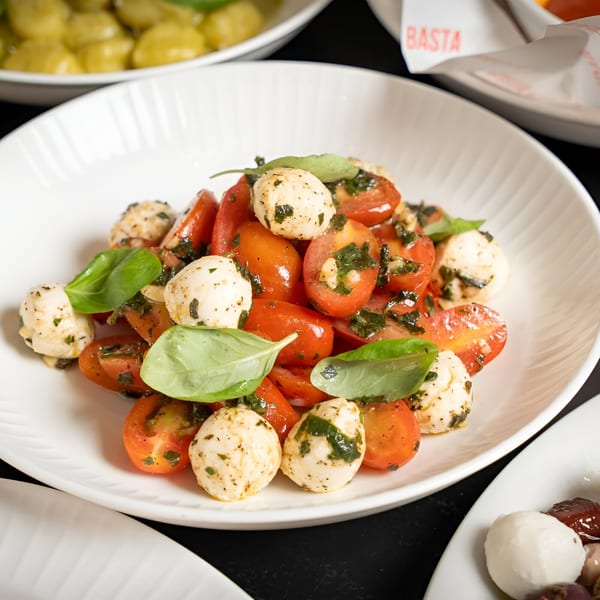 A white bowl of Italian caprese salad with cherry tomatoes, mozzarella balls, and fresh basil.