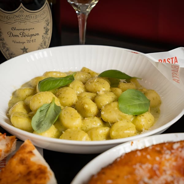 BASTA Pasteria's gnocchi with pesto and basil, with a bottle of Dom Pérignon in the background.