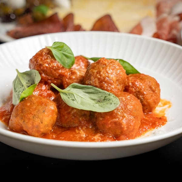 Italian meatballs in red sauce with fresh basil leaves, served in a white bowl.