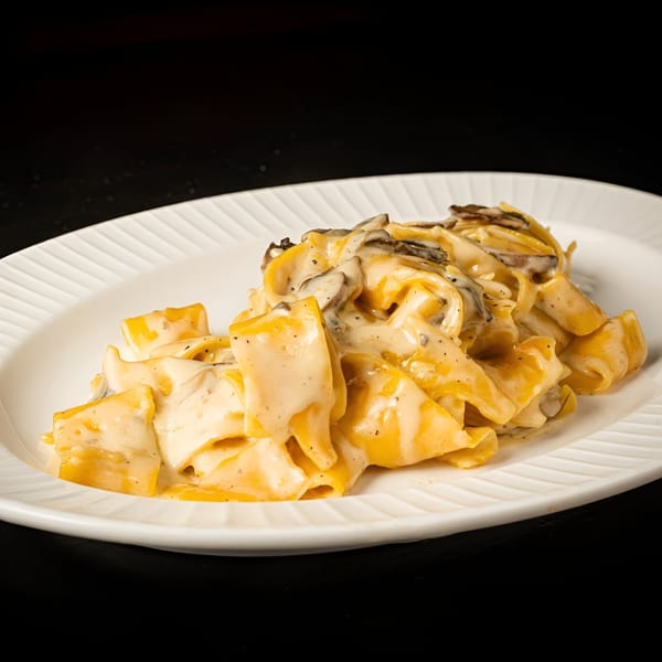 BASTA Pasteria's creamy mushroom pappardelle pasta on a white oval plate against a dark background.